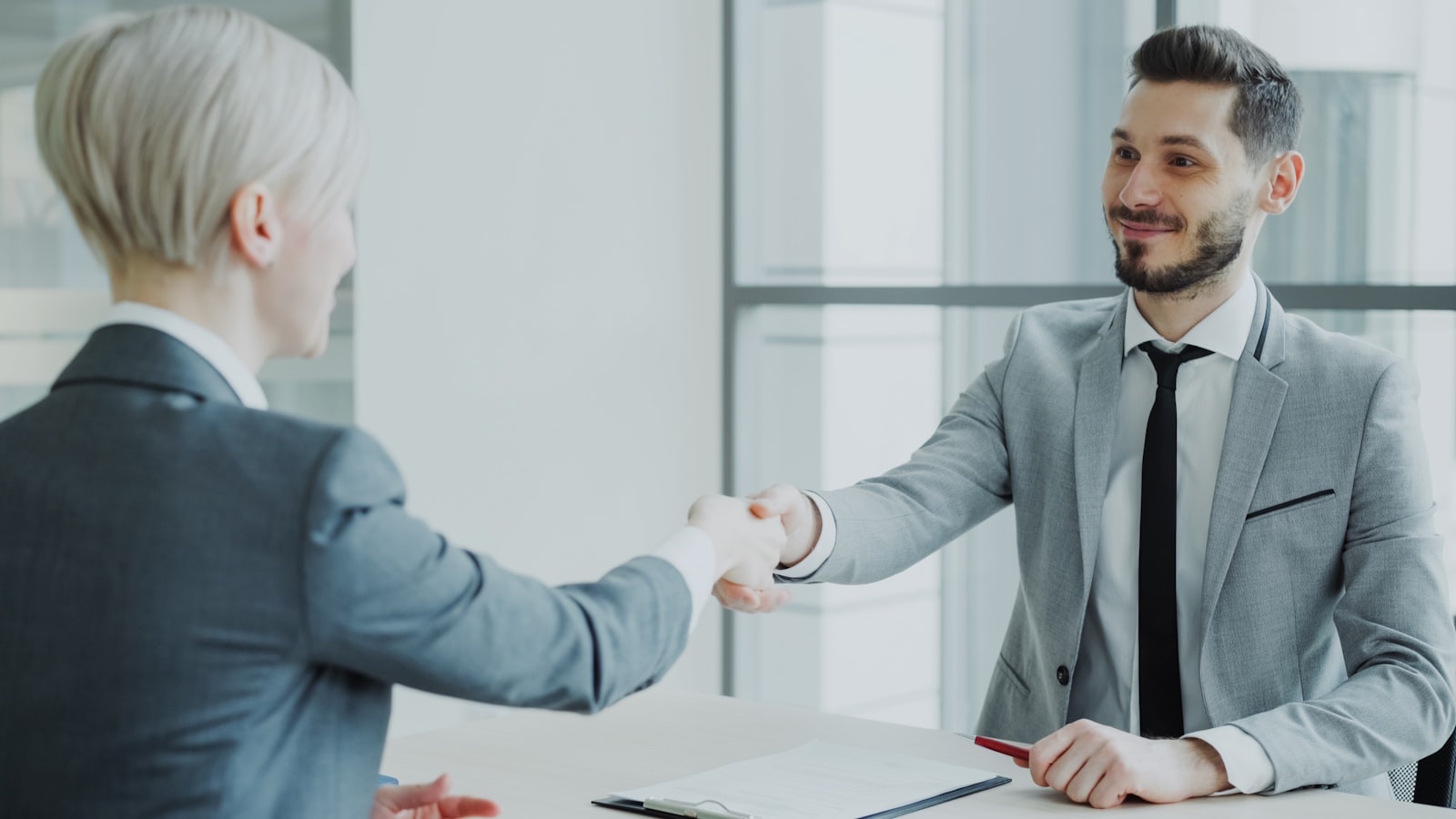 Two professionals shaking hands across a table at the end of a job interview